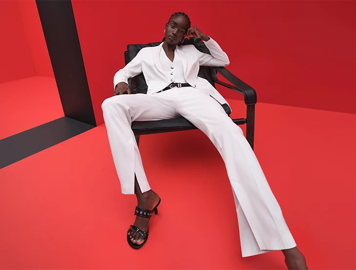 A female model posing in front of a red background wearing white ladies suite (photo)