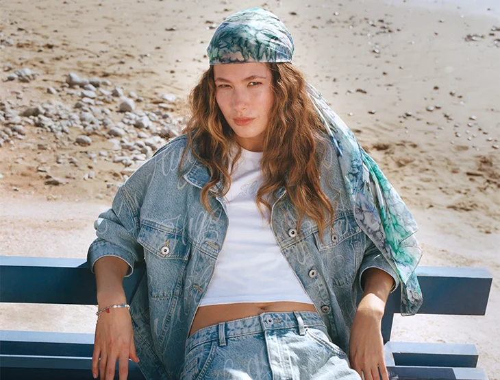 A female model posing on the beach on a bench wearing jeans clothing (photo)