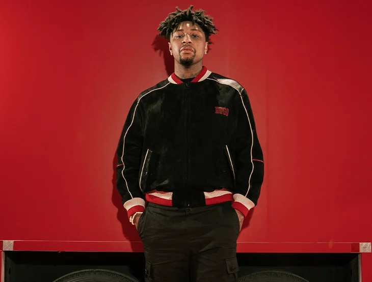 A male model posing in front of a red background in a sporty jacket (photo)