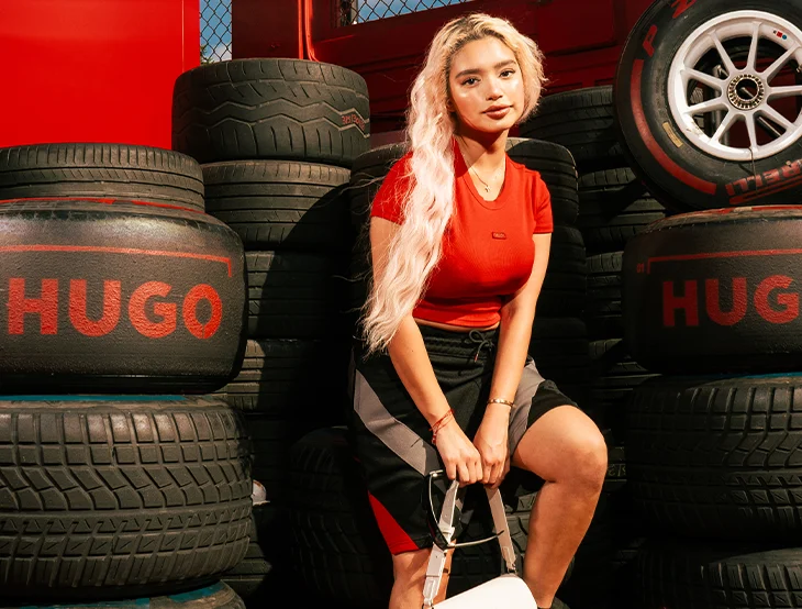 A female model posing in front of black tyres wearing a red Hugo Boss t-shirt (photo)