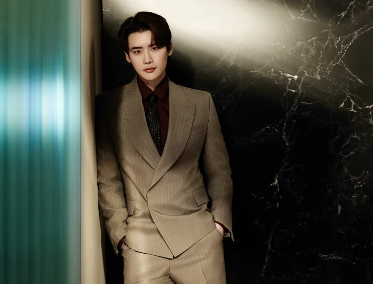 A male model posing in front of a dark background in a sand-colored suit (photo)